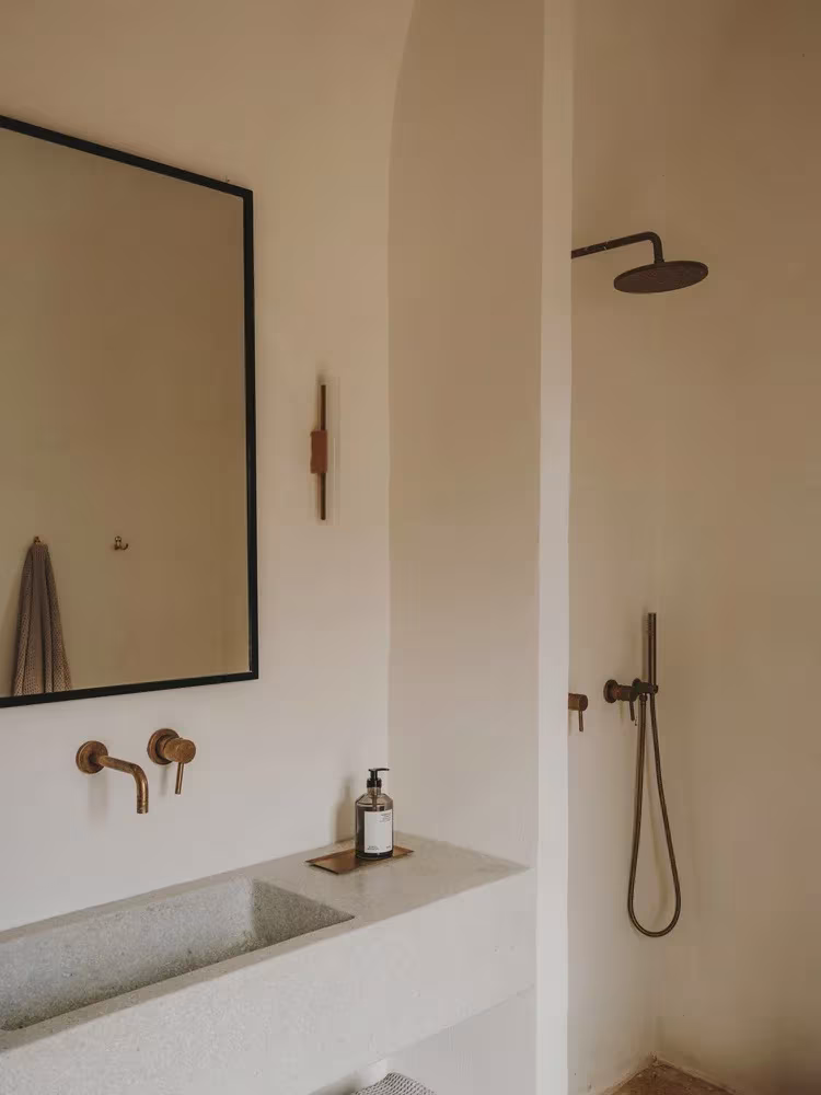 Baño con ducha de latón, espejo enmarcado en negro y lavabo de piedra en la Casa Casolare Scarani