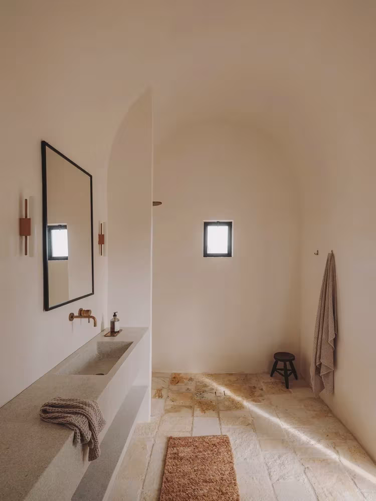 Baño abovedado con lavabo corrido de piedra, espejo negro y suelo de losas en la Casa Casolare Scarani