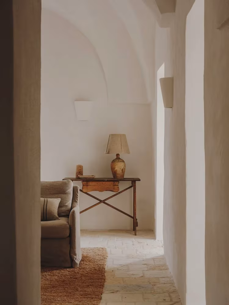 Pasillo de cal blanca con vista a un rincón con escritorio y sillón en la Casa Casolare Scarani
