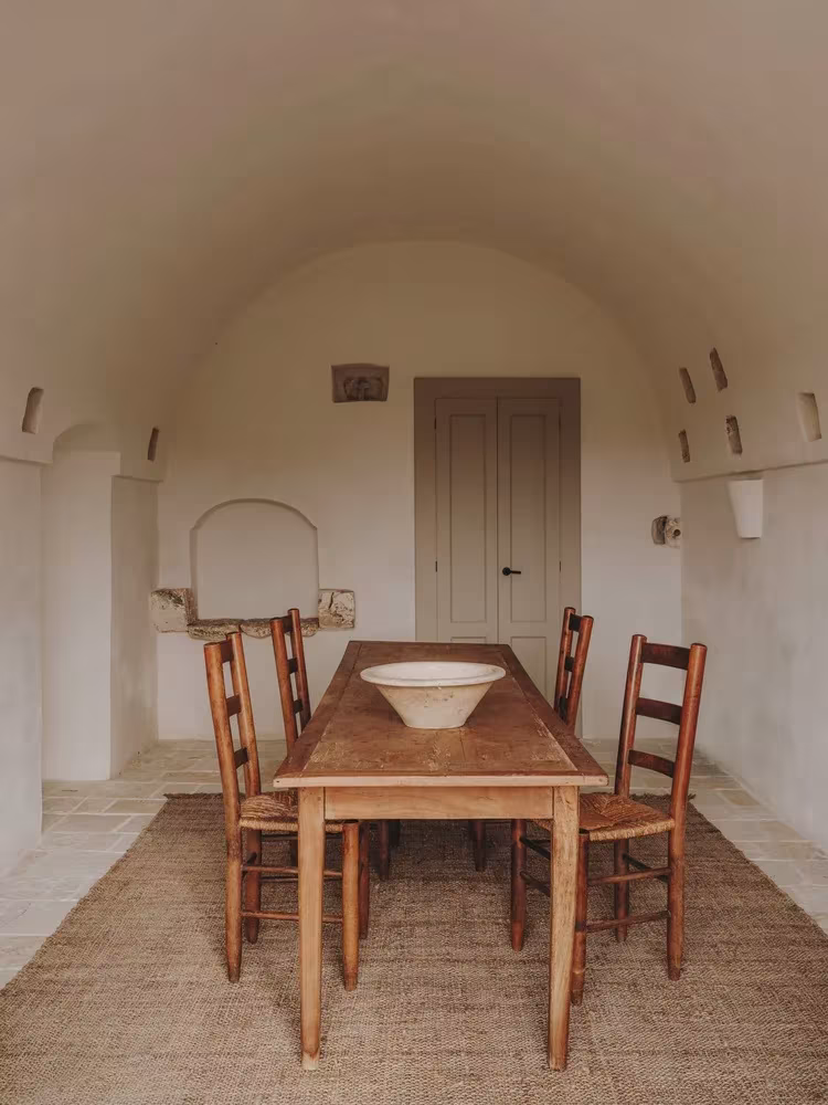Comedor bajo bóveda de cañón con mesa y sillas de madera y alfombra de esparto en la Casa Casolare Scarani