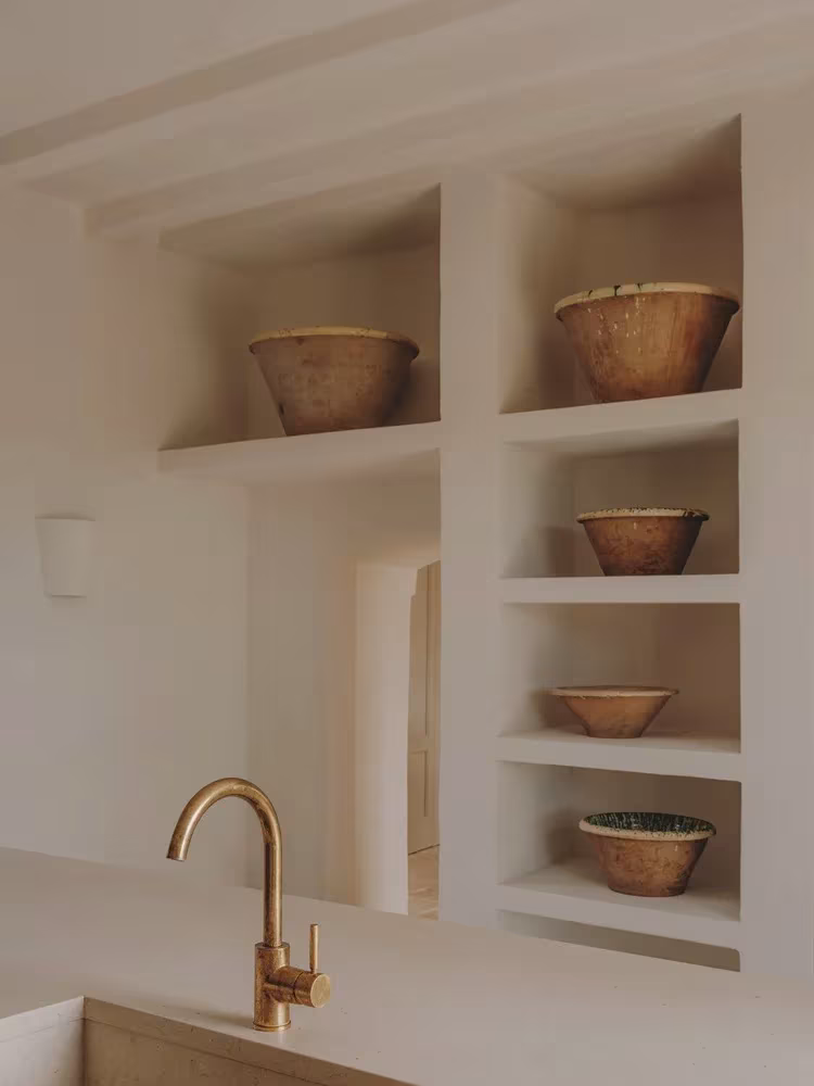 Estantes de obra blanqueada con cuencos de barro y grifería de latón en la cocina de la Casa Casolare Scarani