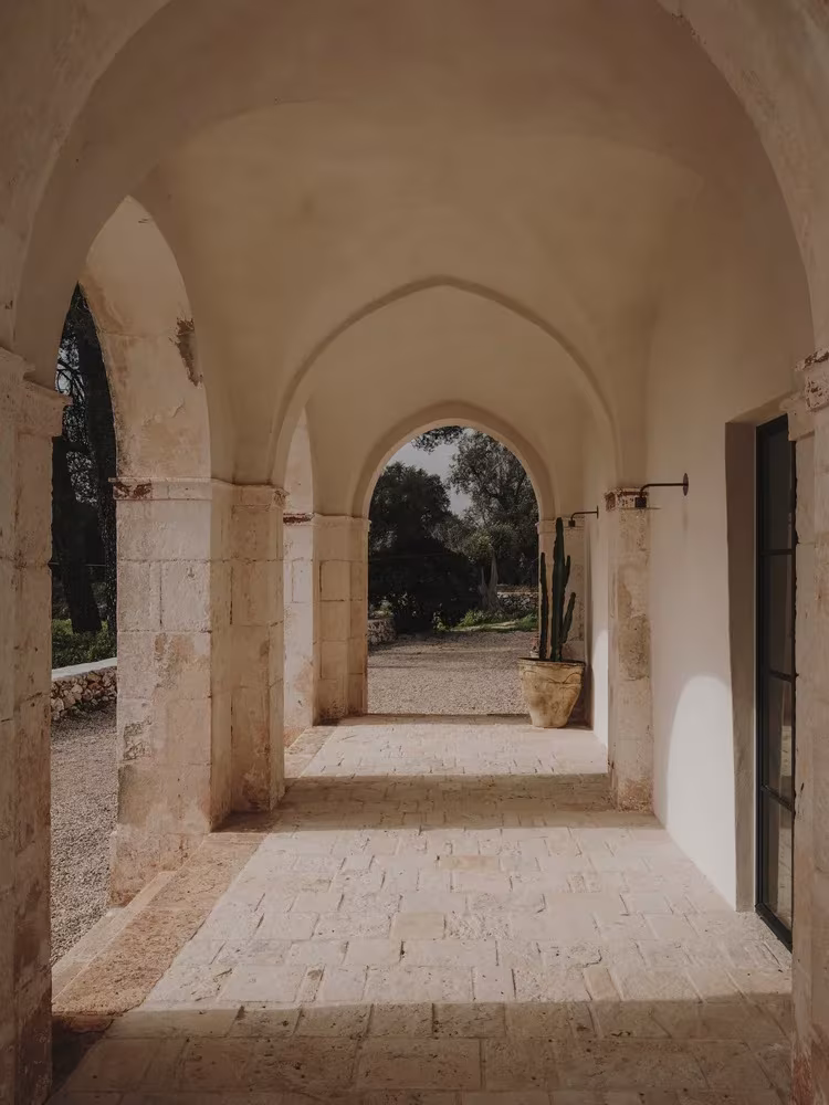 Galería abovedada de piedra con arcos y suelo de losas que se abre al jardín en la Casa Casolare Scarani