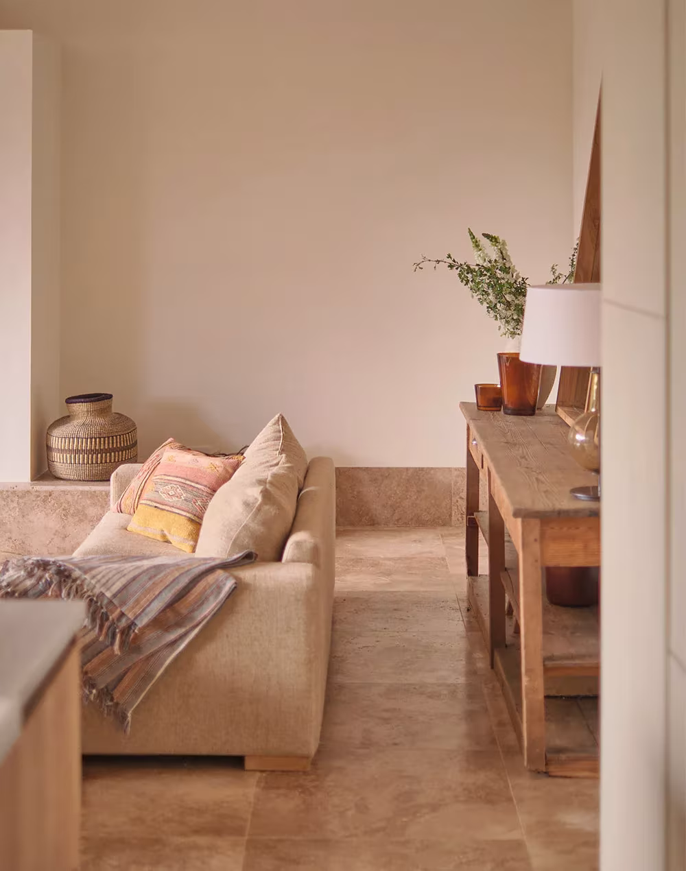 Rincón de lectura con sofá, consola de madera y lámpara de mesa sobre suelo de travertino en la Cabaña en la Vera