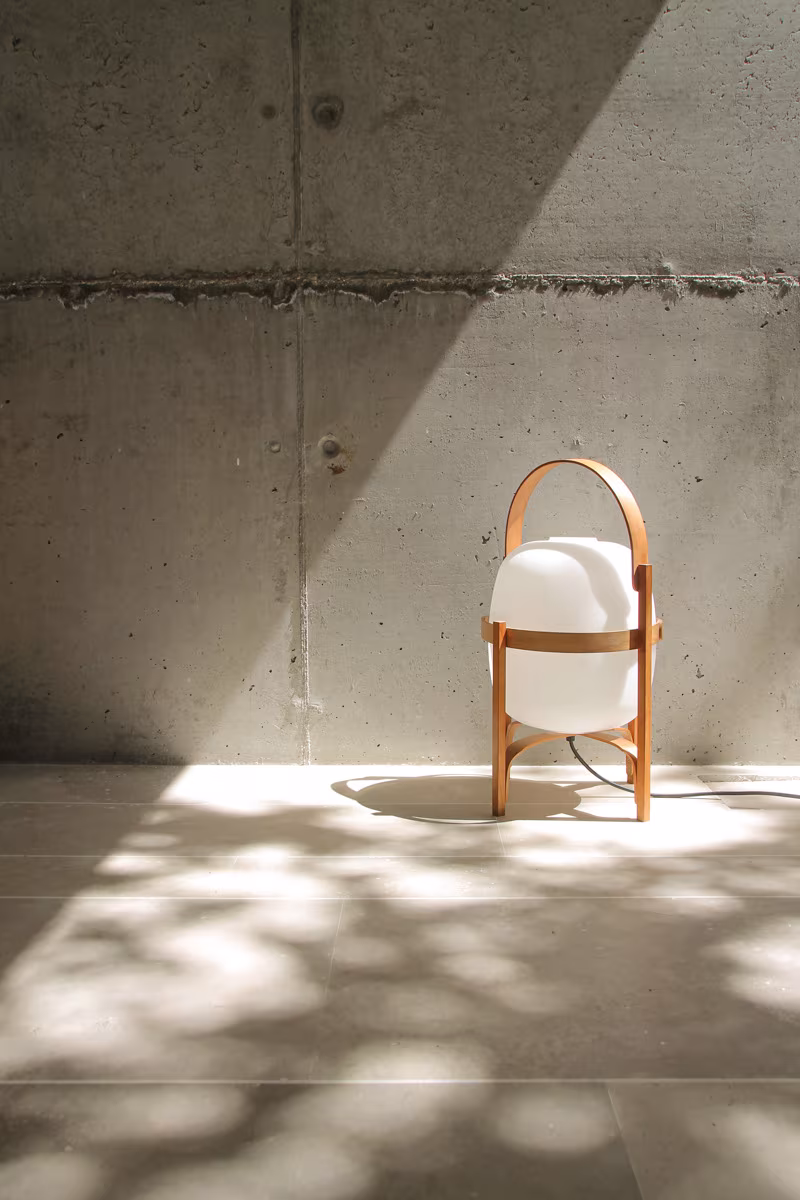 Portable timber and opal lamp on a stone floor before a concrete wall with dappled light, Ábaton studio