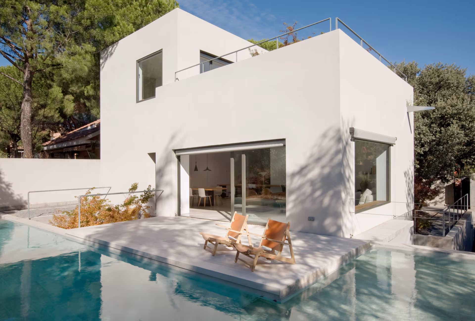 White volume with terrace and stone-edged pool holding two loungers, Ábaton studio