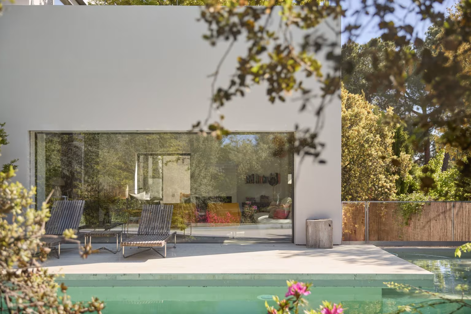 Volumen blanco con gran cristalera abierto a una piscina y a una terraza con tumbonas, del estudio de Ábaton