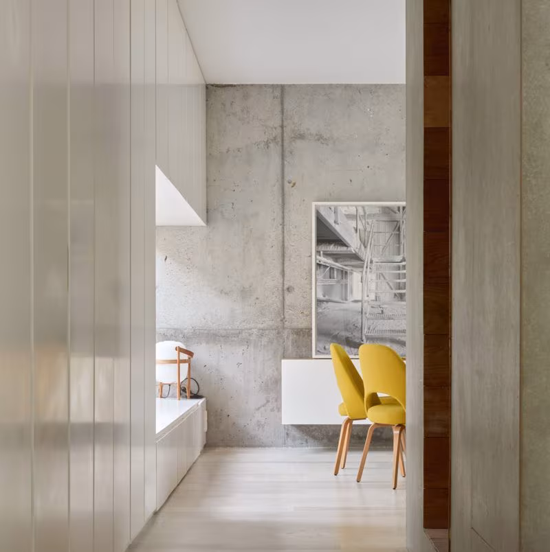Exposed concrete wall and pale timber panels with yellow chairs beyond, Ábaton studio
