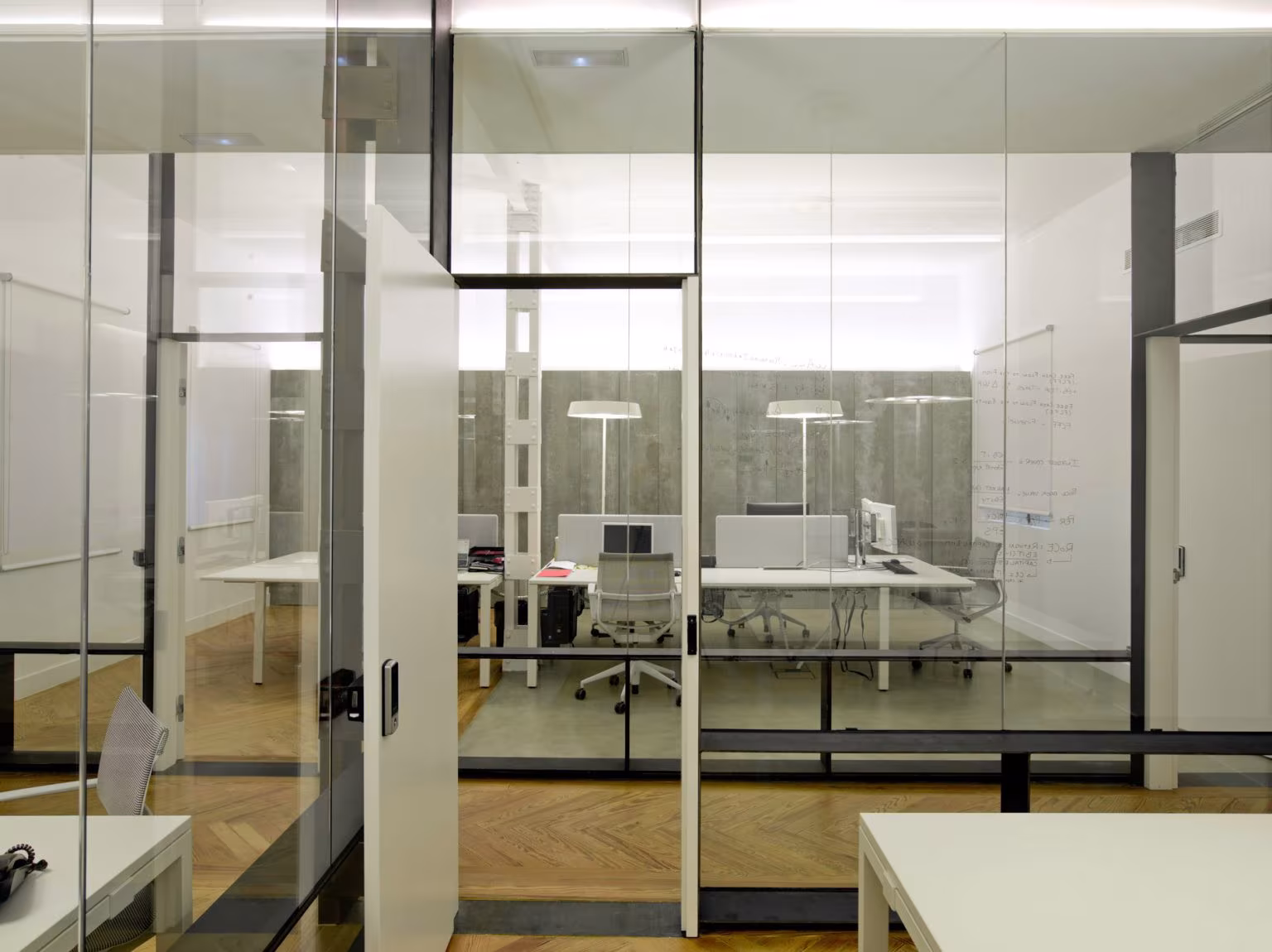 Office seen through double glass partitions with dark frames and a whiteboard beyond, Oficina ED