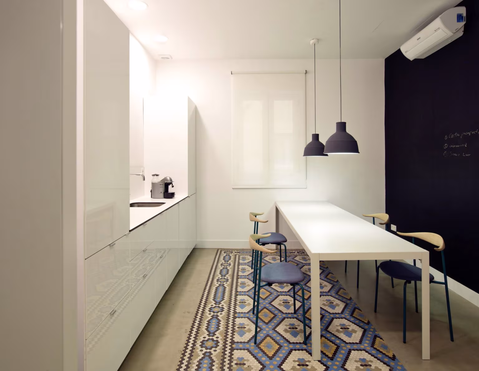 Staff kitchen with linear white units, high table, black pendants and encaustic tile floor, Oficina ED