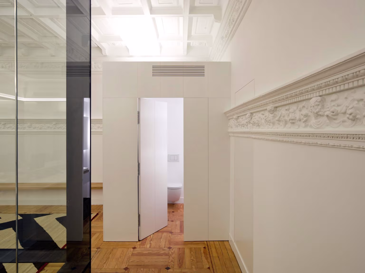 Corridor with decorated plaster dado, white partition with door and parquet floor, Oficina ED by Ábaton