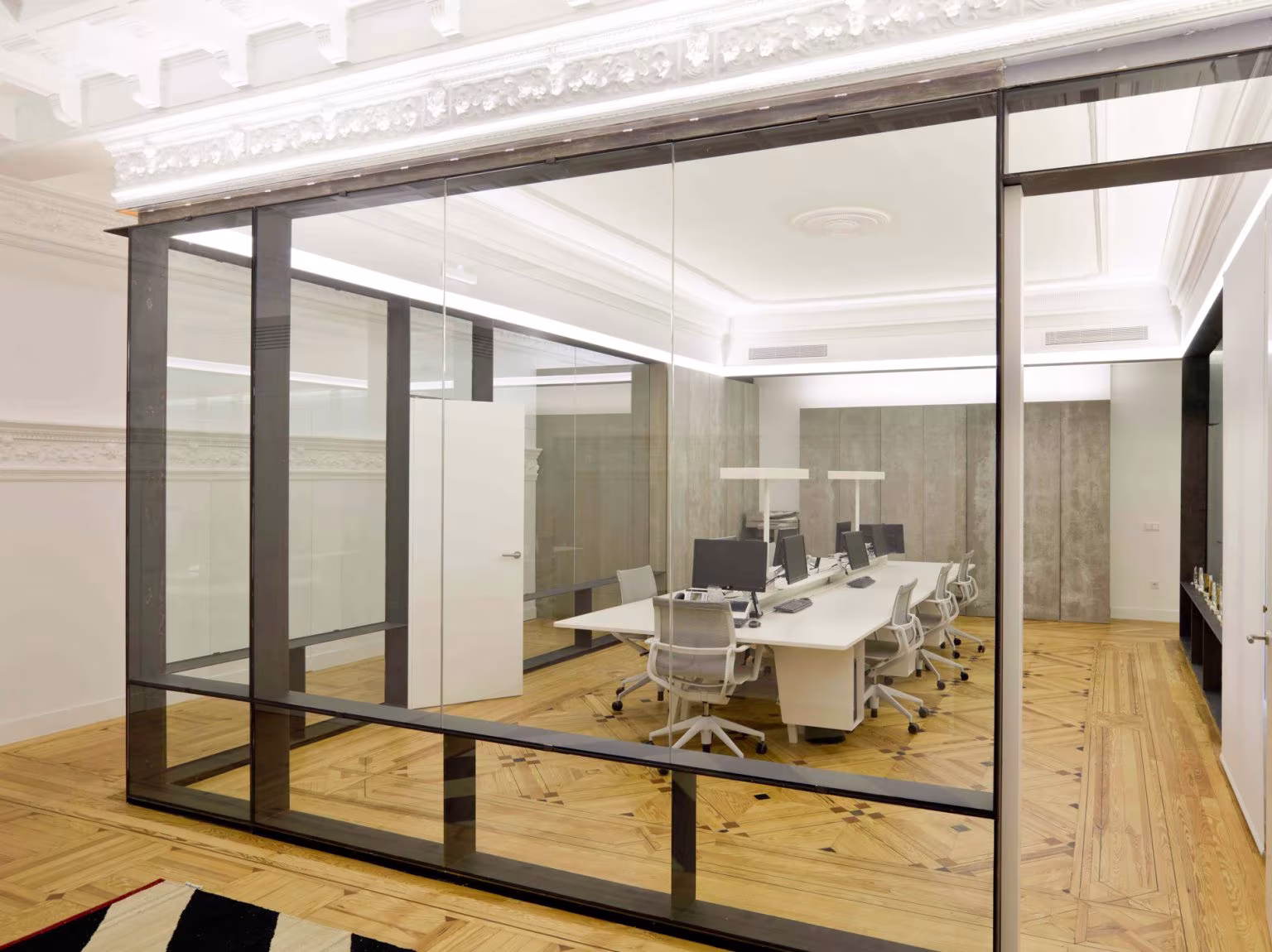 Sala de oficina acristalada con mesa de trabajo blanca y molduras clásicas en el techo en la Oficina ED de Ábaton
