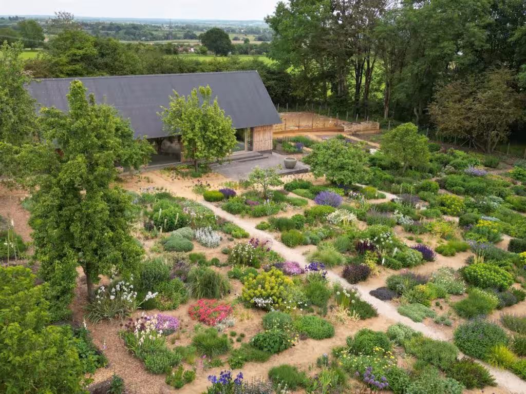 Vista aérea del jardín de Serge Hill Project con parterres naturalistas y senderos junto a la casa de tejado oscuro