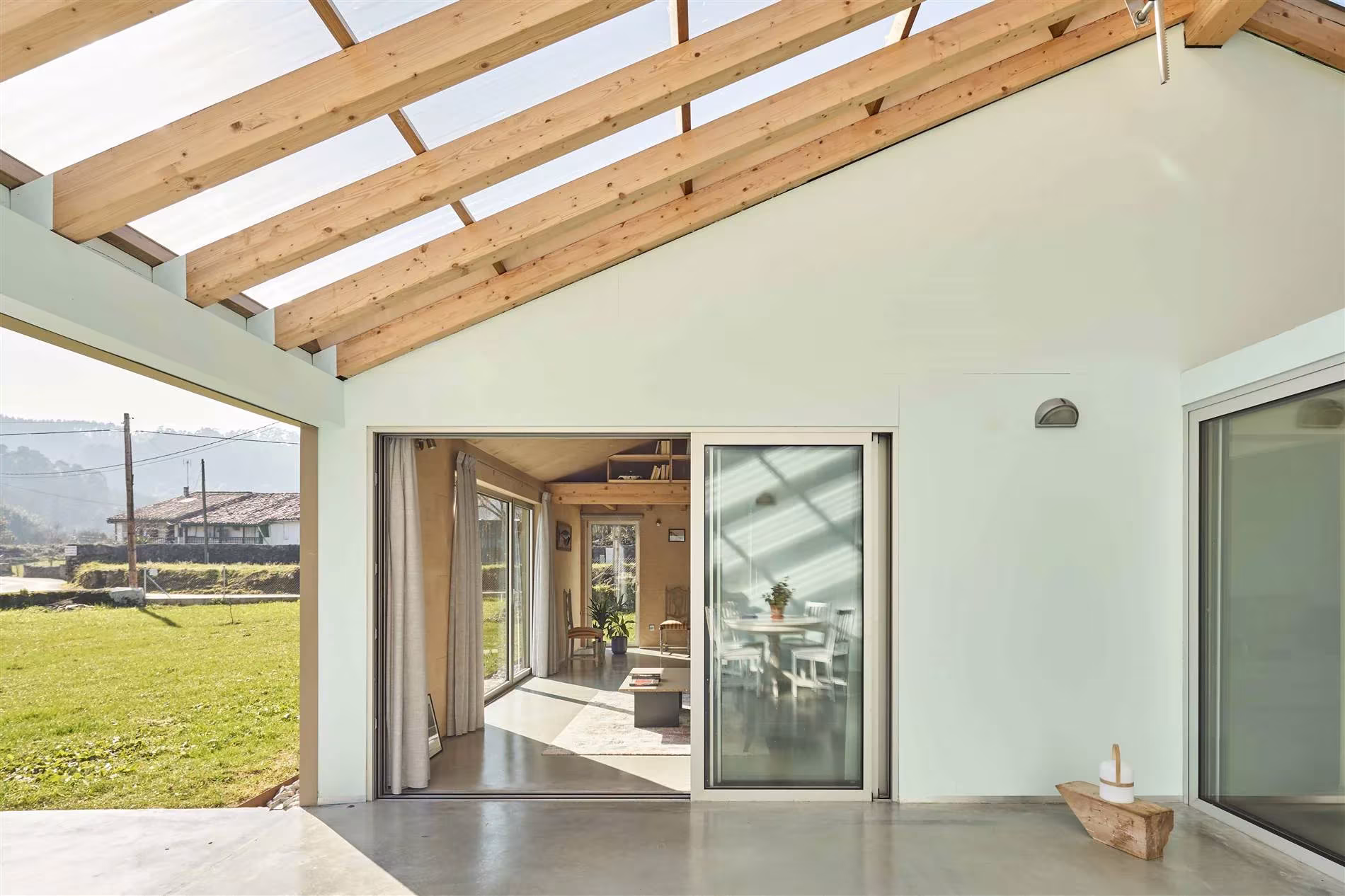 Interior de la casa invernadero de Navajeda con vigas de madera y paneles translúcidos abiertos al jardín