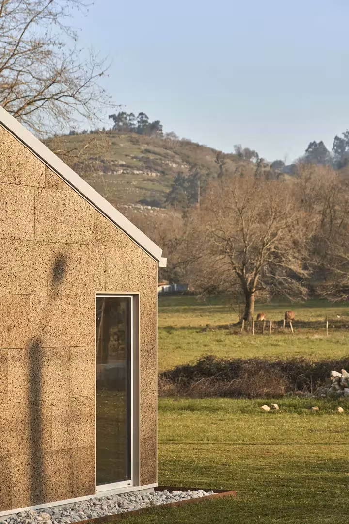 Testero de corcho de la casa de Navajeda con ventana vertical, ante un prado y una colina arbolada
