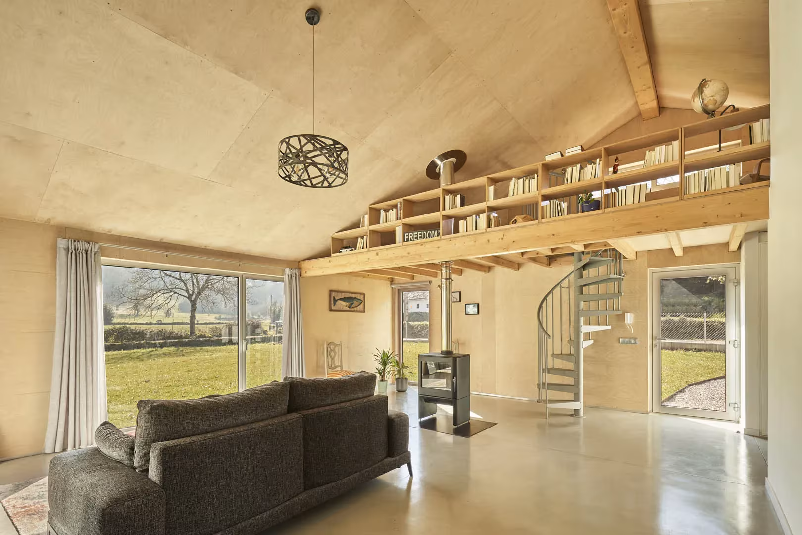 Salón a doble altura de la casa de Navajeda con revestimiento de madera, biblioteca en altillo y escalera de caracol