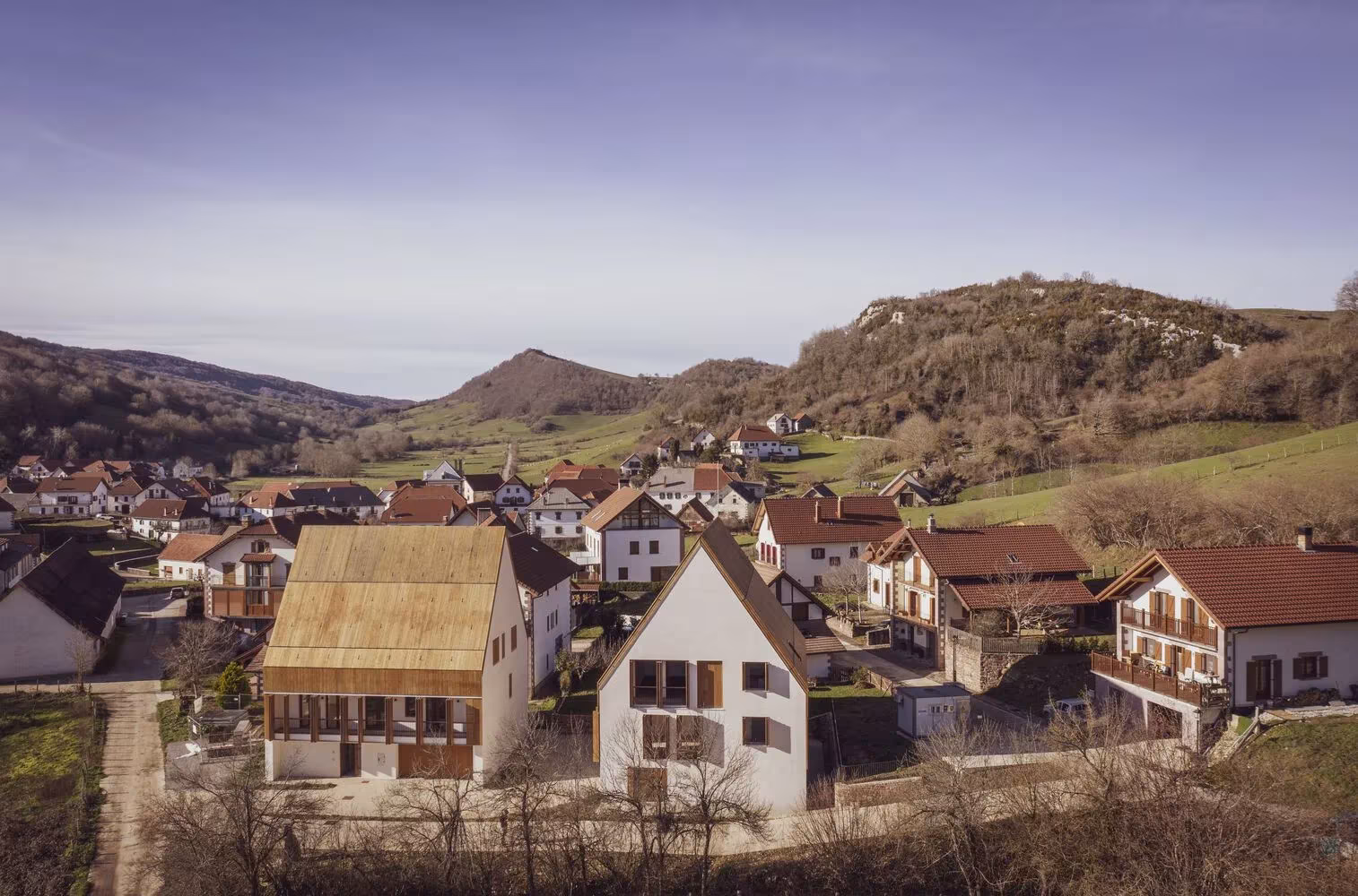 Vista aérea del conjunto de caseríos de madera junto al pueblo, con montañas al fondo
