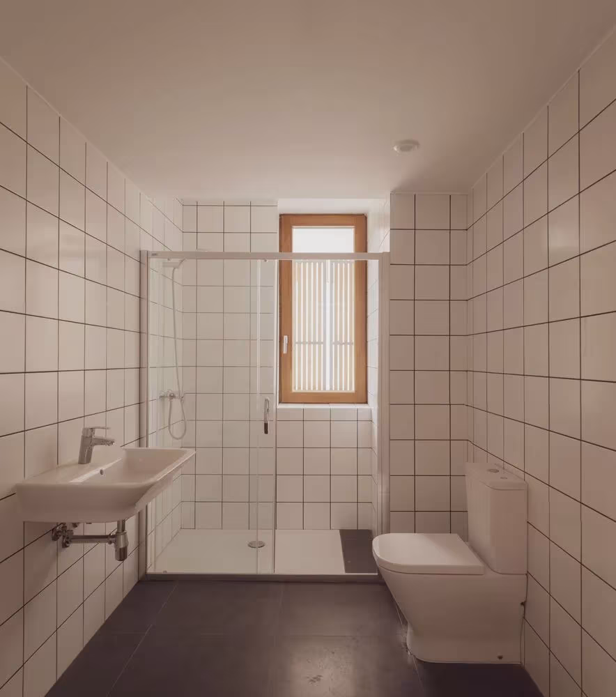 Baño de los caseríos de CLT con azulejo blanco, ducha acristalada y ventana de madera vertical