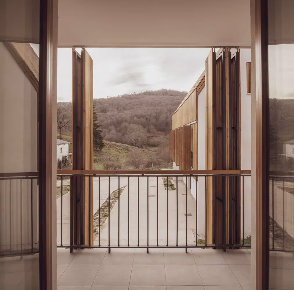 Balcón con contraventanas de madera abiertas y barandilla metálica con vistas al monte y al patio