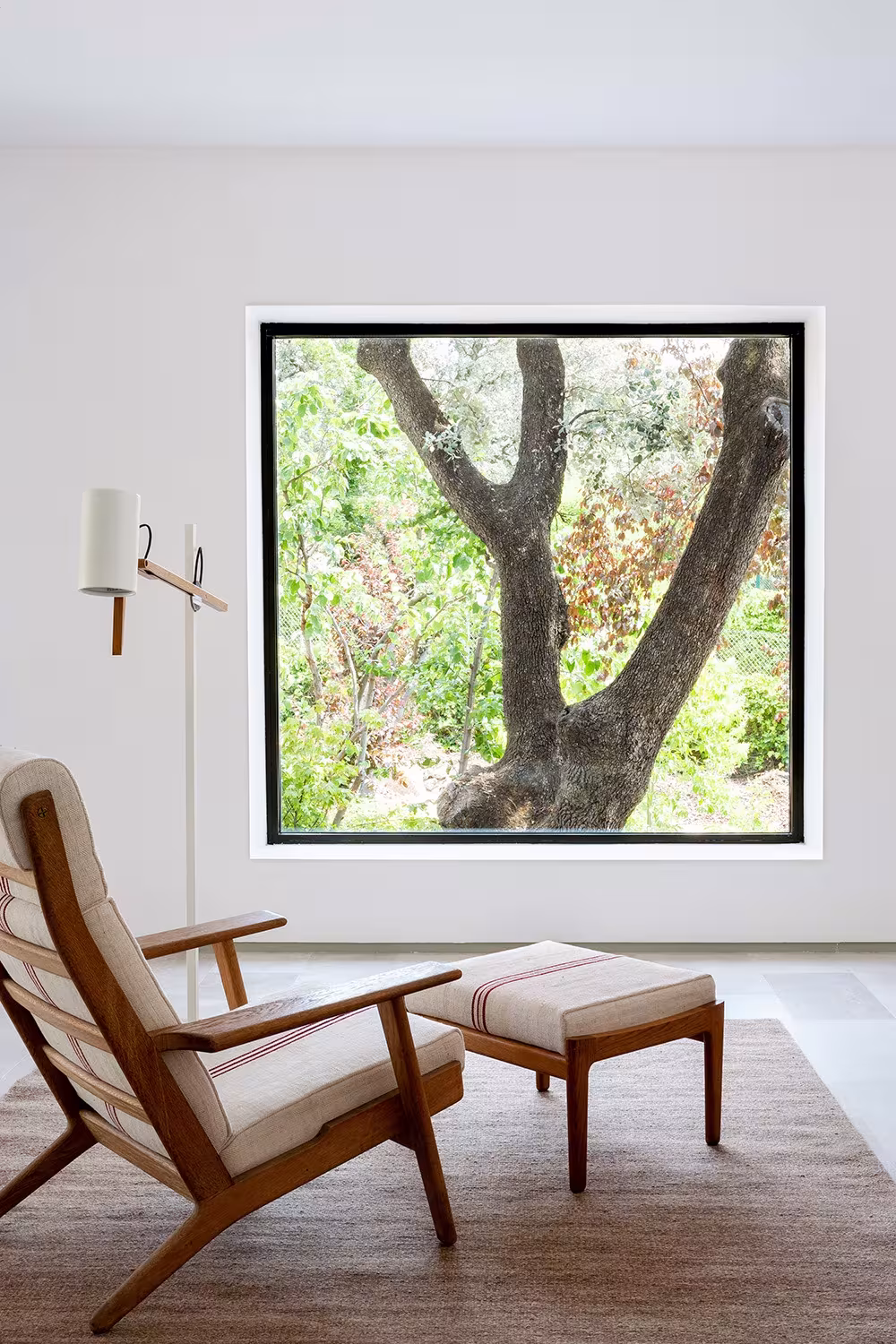 La Moraleja-ABATON-13 Square window framing an oak tree beside a timber armchair with ottoman, La Moraleja, Madrid