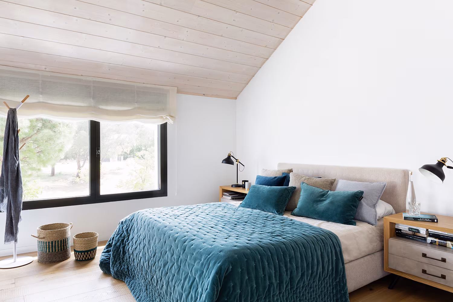 Bedroom under a sloping ceiling with turquoise bedspread, baskets and a window to the woodland, Proyecto XY