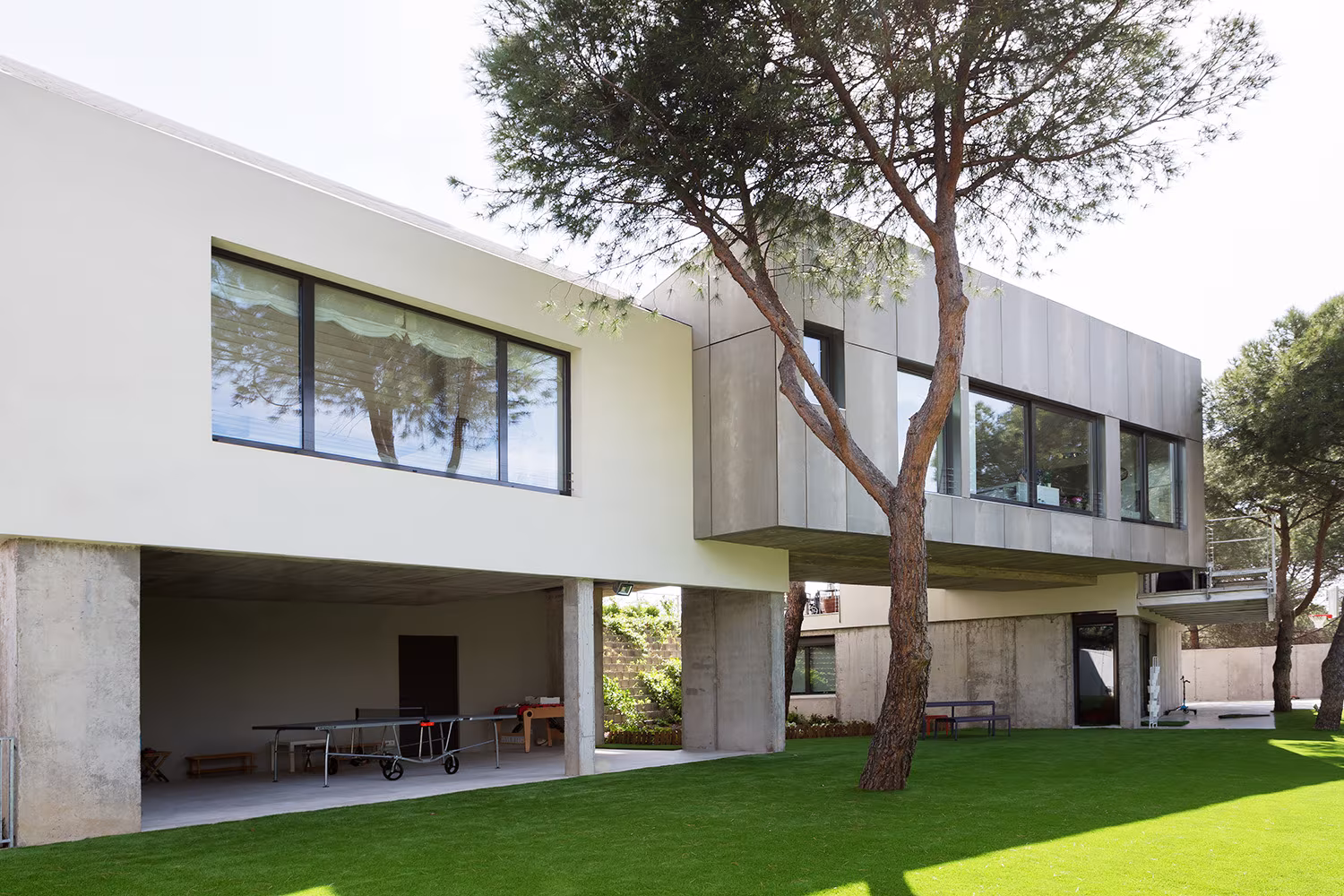 Upper volume clad in metal on concrete pillars beside a pine tree, Proyecto XY