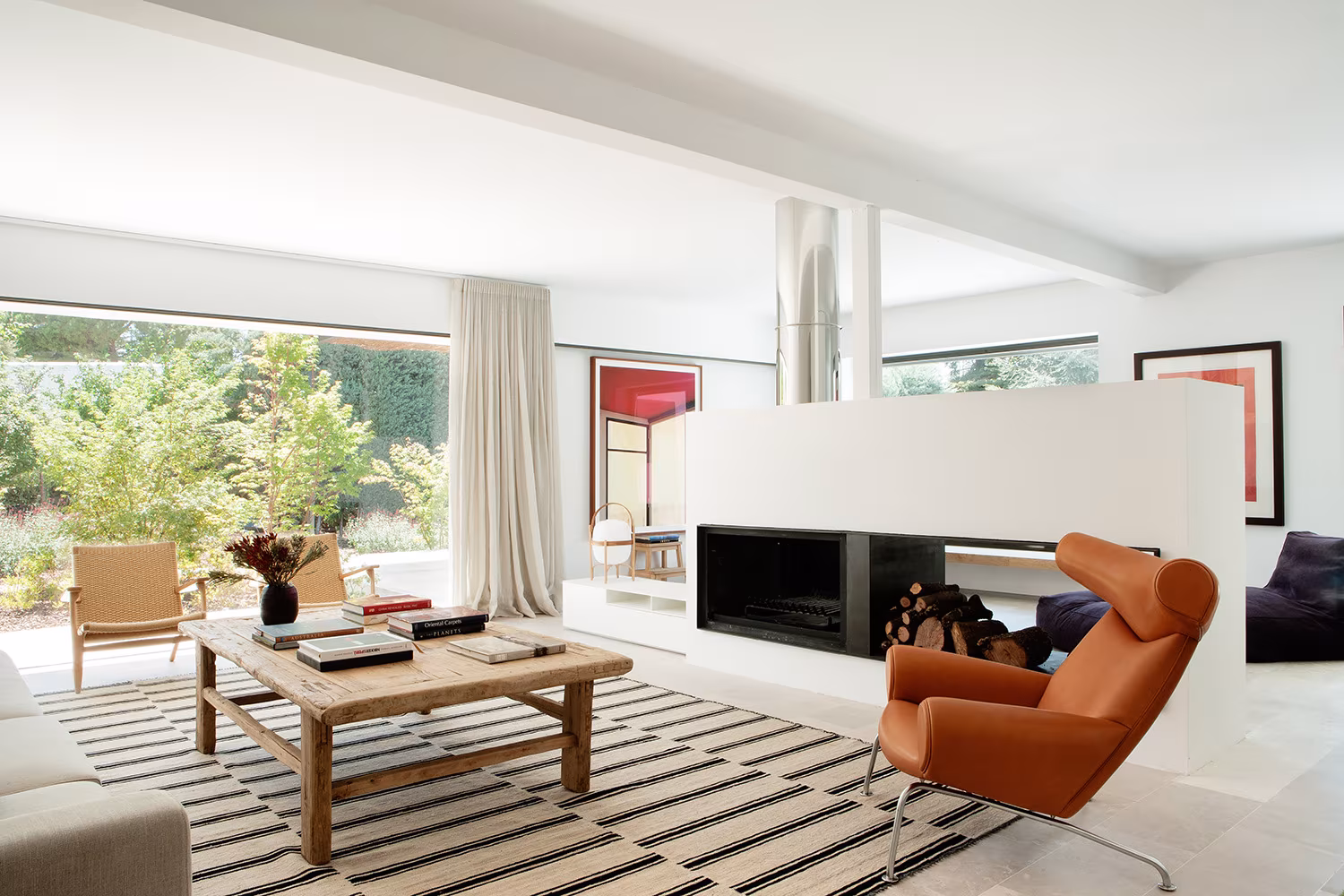 Living room with white central fireplace, orange armchair and large garden window, La Moraleja refurbishment