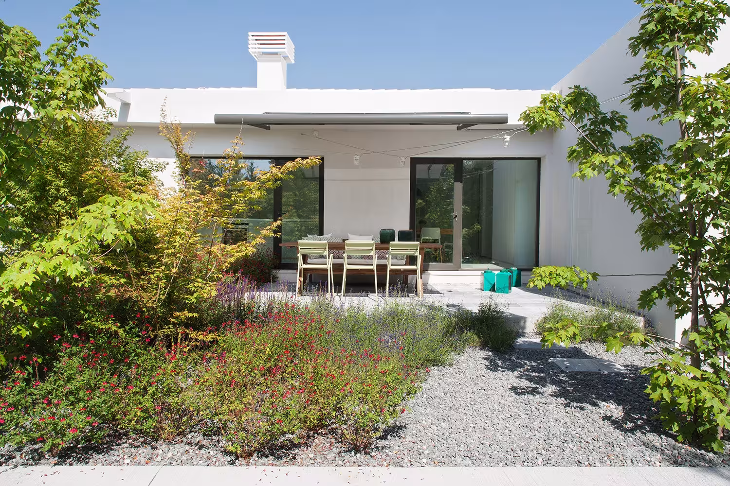 Gravel and perennial garden before the white façade and the terrace with dining table, La Moraleja, Madrid