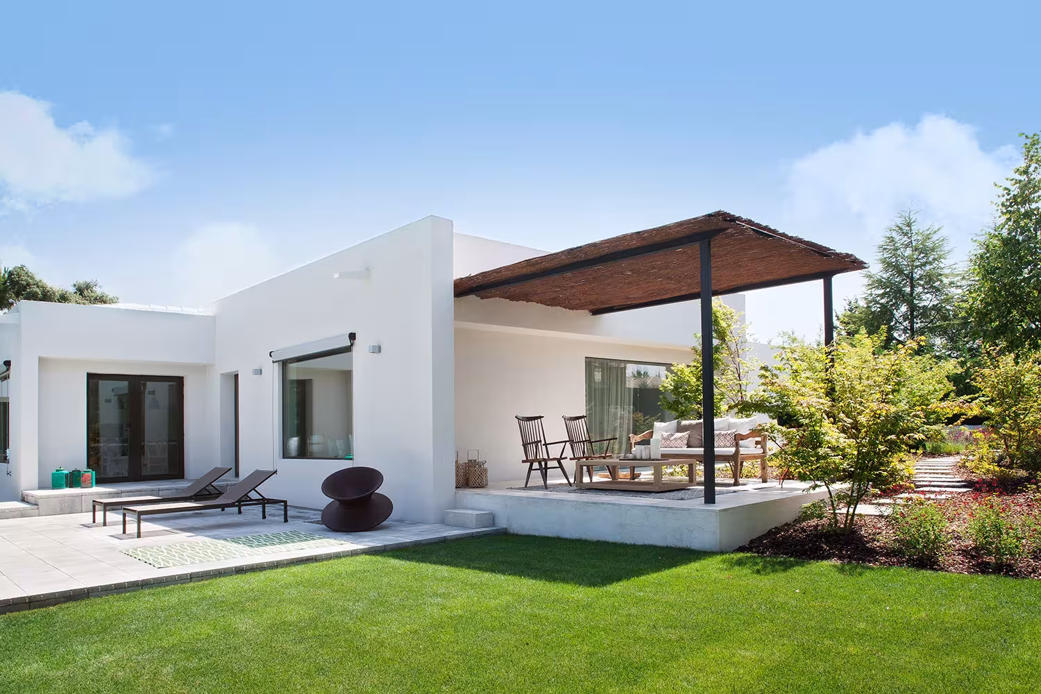 Raised terrace with pergola, loungers and shrubs beside the lawn, La Moraleja refurbishment