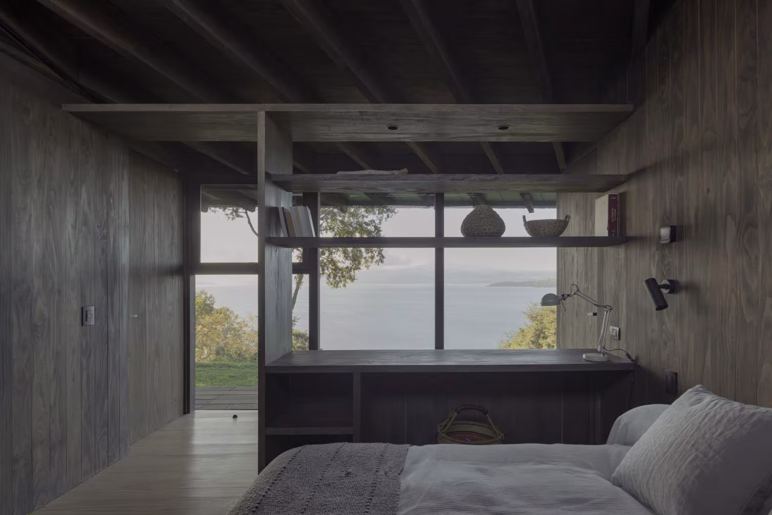 Dormitorio con la cama frente a una ventana con vistas al lago y paramentos de madera en Casa Puerto Nuevo