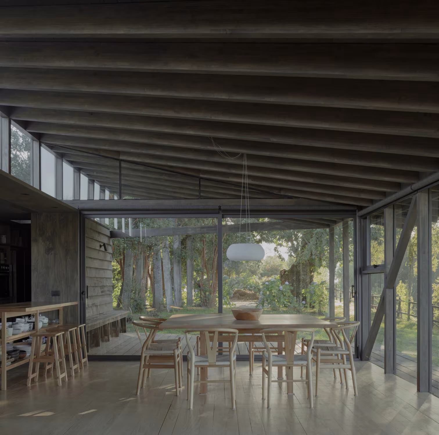 Comedor con mesa larga y sillas de madera bajo la estructura ligera de vigas oscuras de Casa Puerto Nuevo