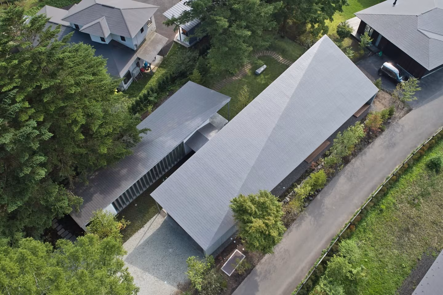 Aerial view of the gabled roof of the Symbiotic House among trees and forest paths