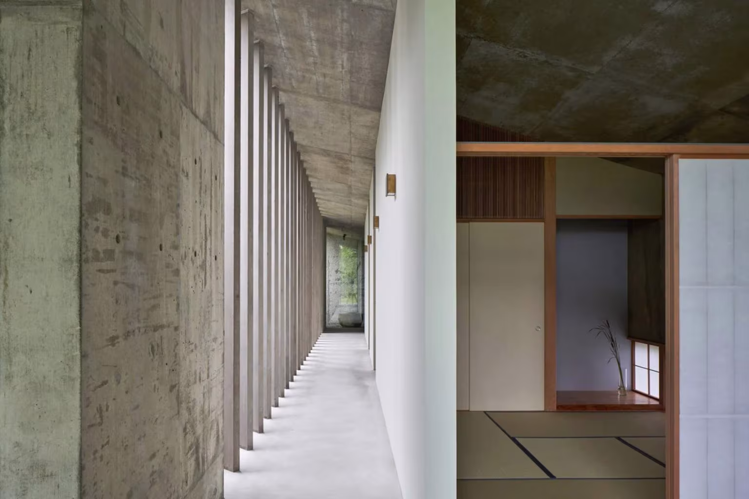 Concrete corridor with slender timber posts and a view into a tatami room in the Symbiotic House