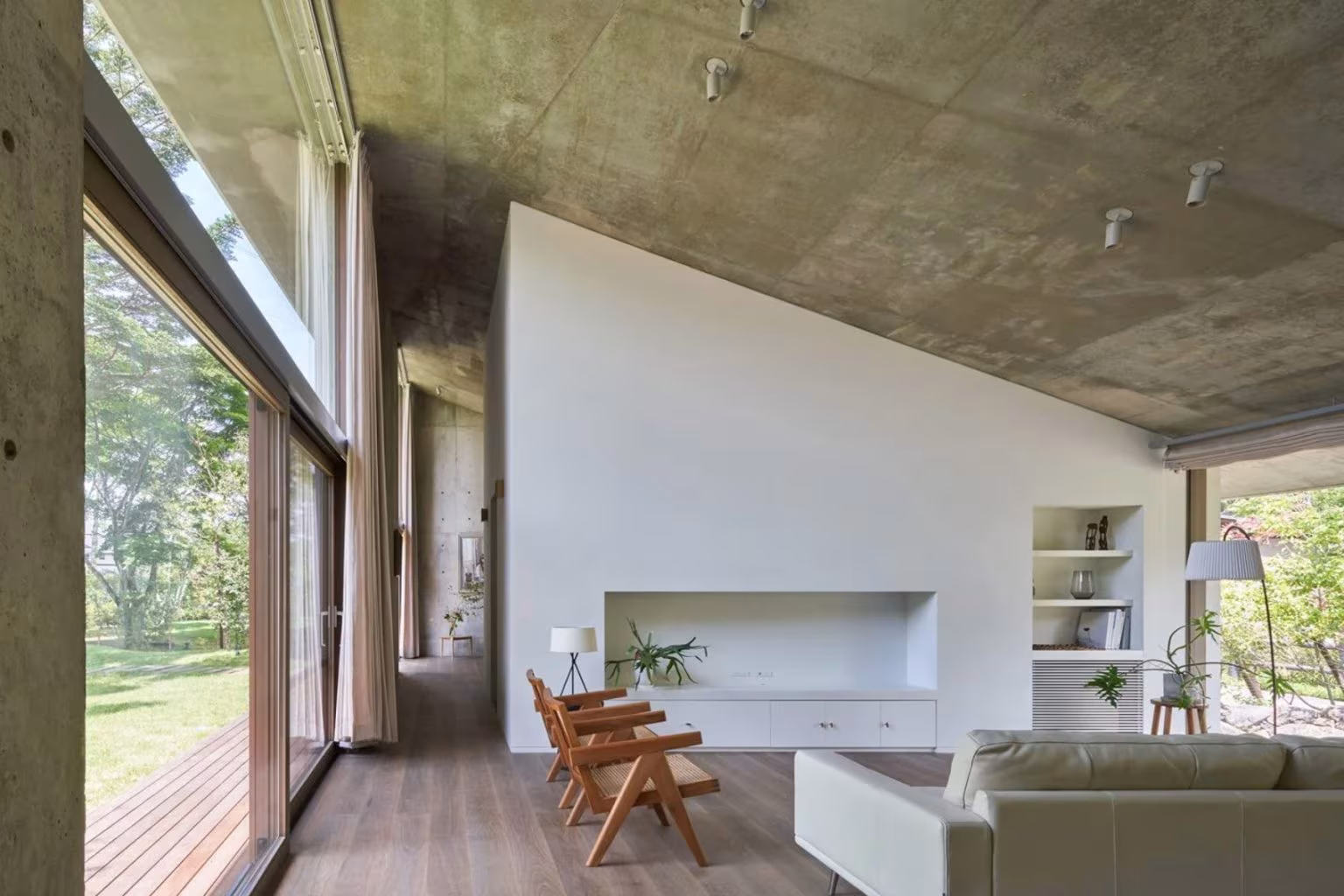 Room with sloping concrete ceiling, built-in fireplace, sofa and timber deck in the Symbiotic House