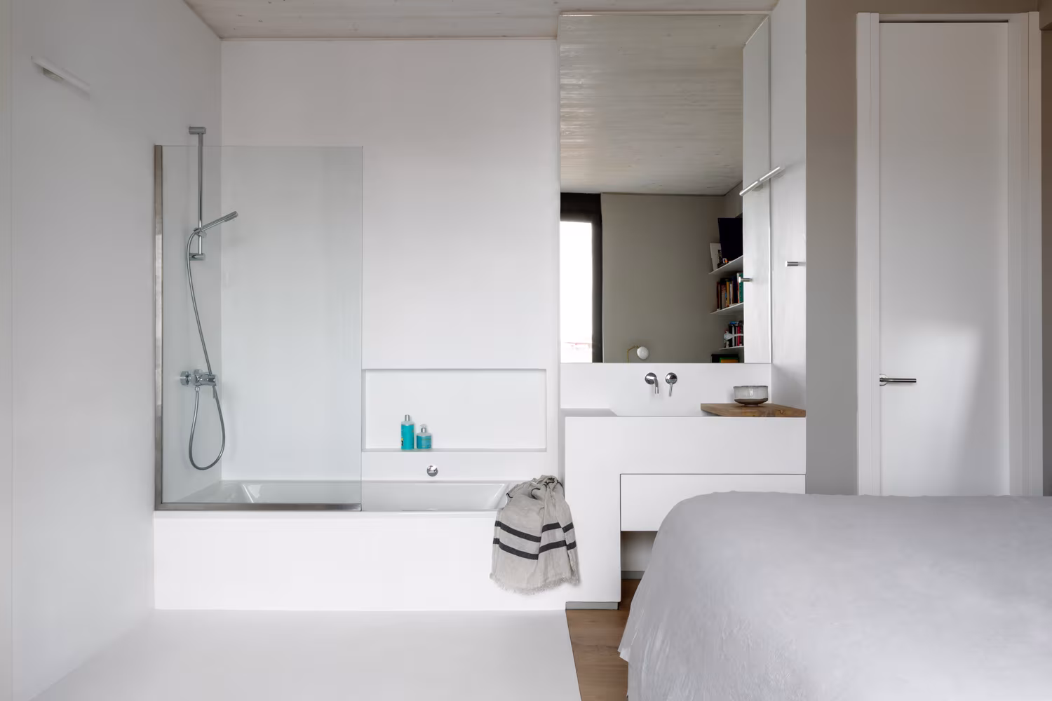 Baño abierto al dormitorio en ARV8, con bañera y ducha tras una mampara de cristal y lavabo suspendido blanco