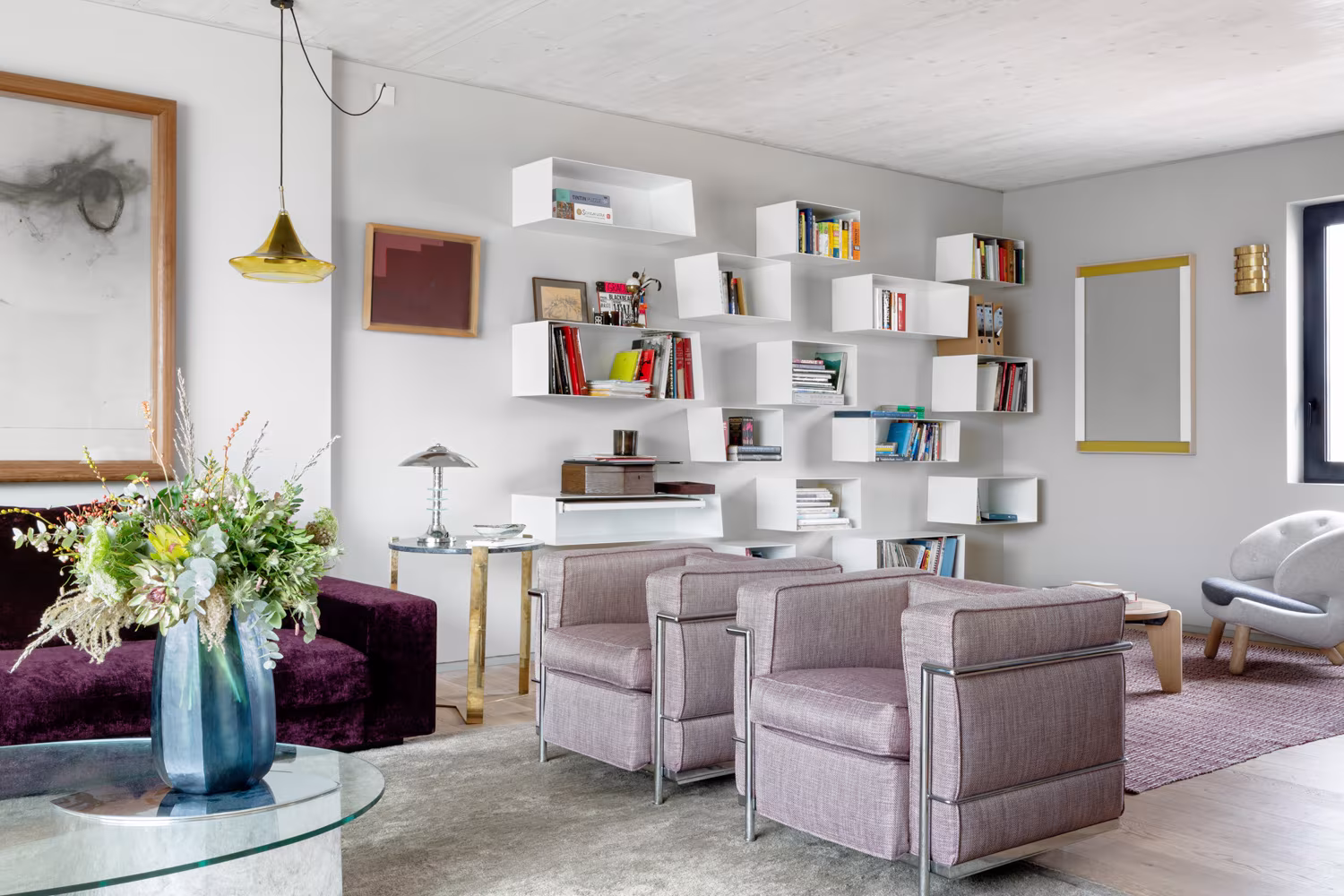 Rincón del salón de ARV8 con estantería blanca de módulos, butacas lavanda y un ramo sobre la mesa baja