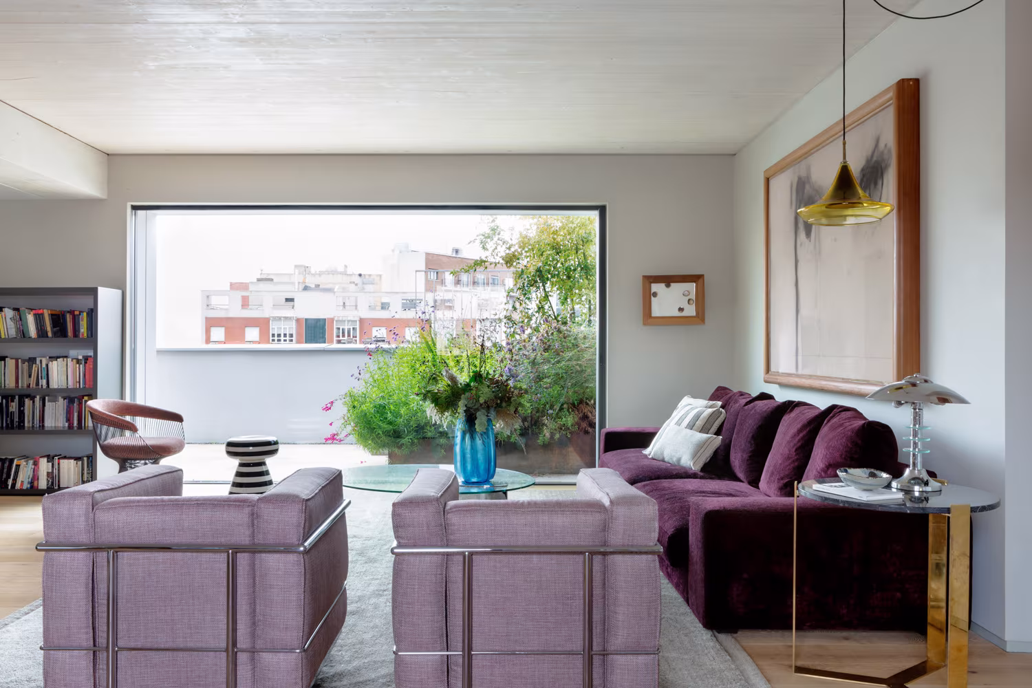 Salón de ARV8 con butacas y sofá púrpura frente a una gran ventana abierta a la terraza y a la ciudad