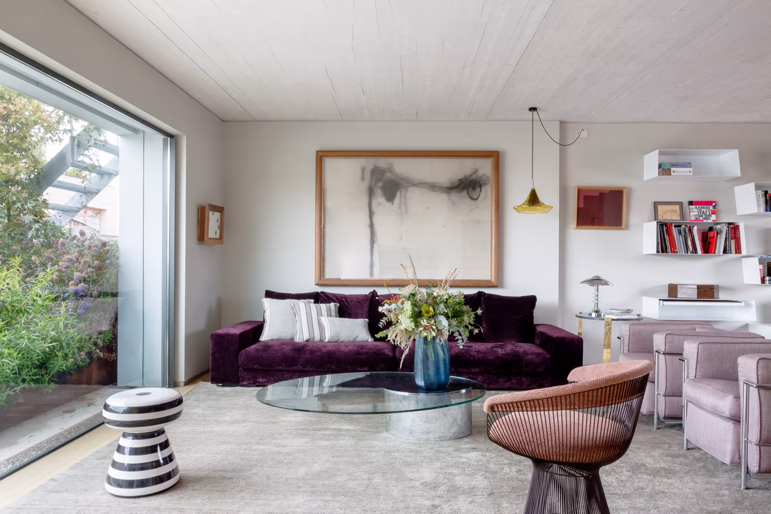 Salón de ARV8 con sofá granate, mesa de centro de cristal y gran ventana a la terraza bajo un techo de madera clara