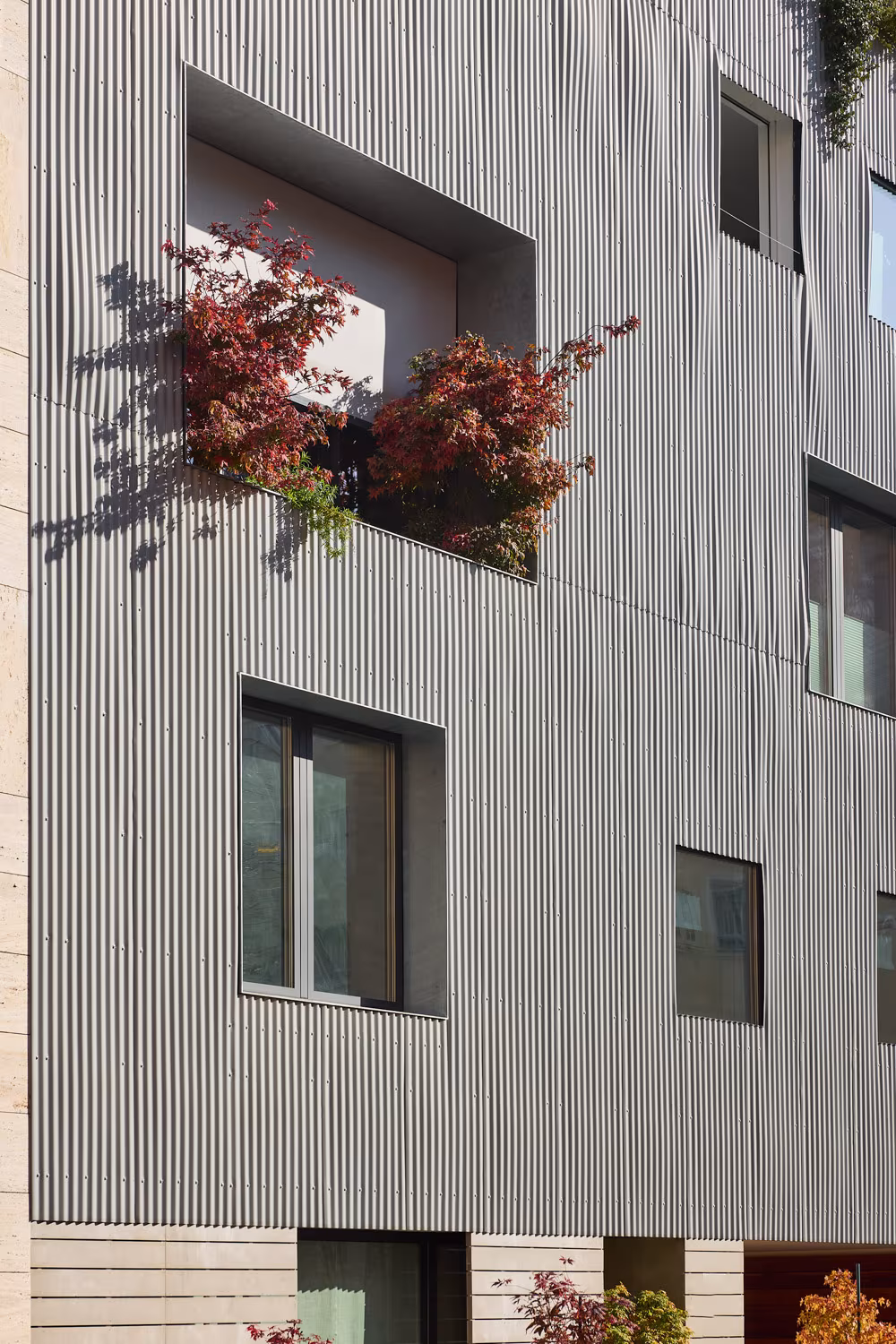 Corrugated metal façade with red maples in a recess, ARV8 building by Ábaton in Madrid
