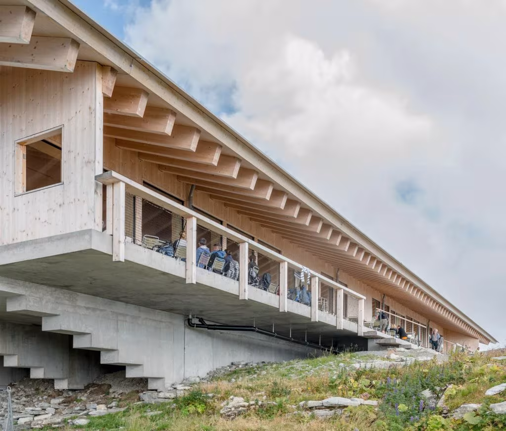 Timber building at Chäserrugg with a cantilevered gallery, exposed rafters and a stair over concrete foundations