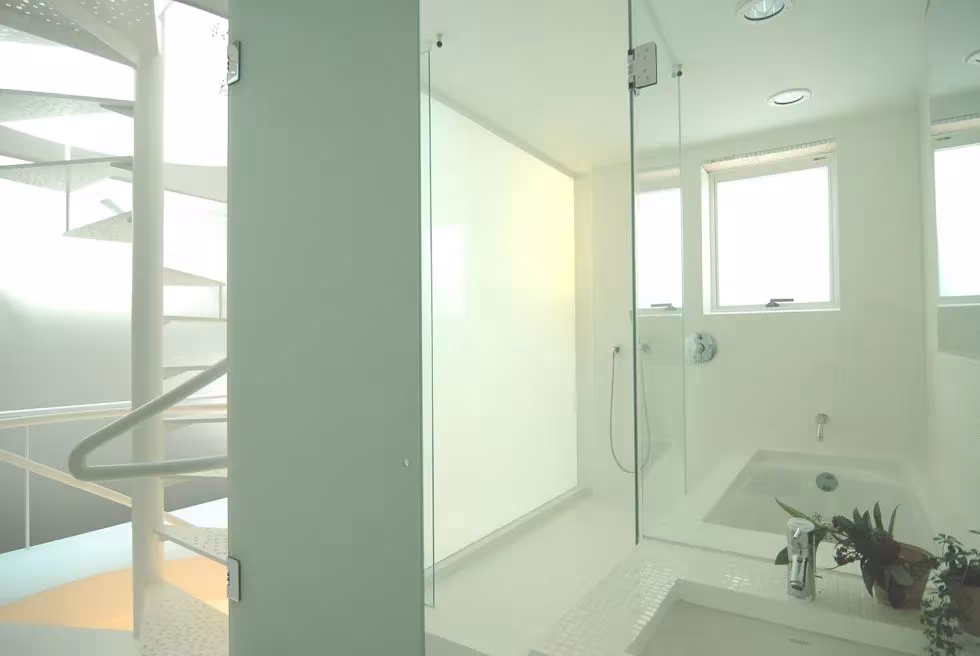 Baño de la House SH con mampara de vidrio translúcido y escalera de caracol blanca al fondo