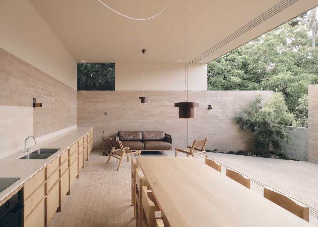 Cocina y salón abiertos de High Street House, de Lineburg Wang, con muro de ladrillo claro y mobiliario de madera