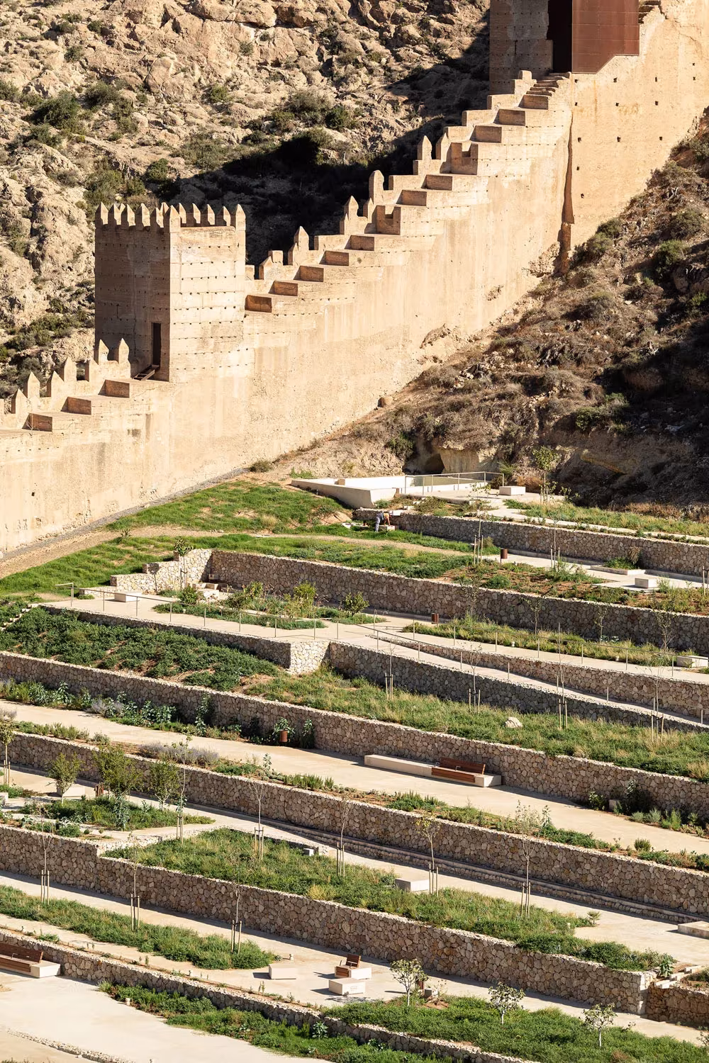 Muralla almenada sobre los bancales aterrazados con plantas mediterráneas del parque de La Hoya, en Almería