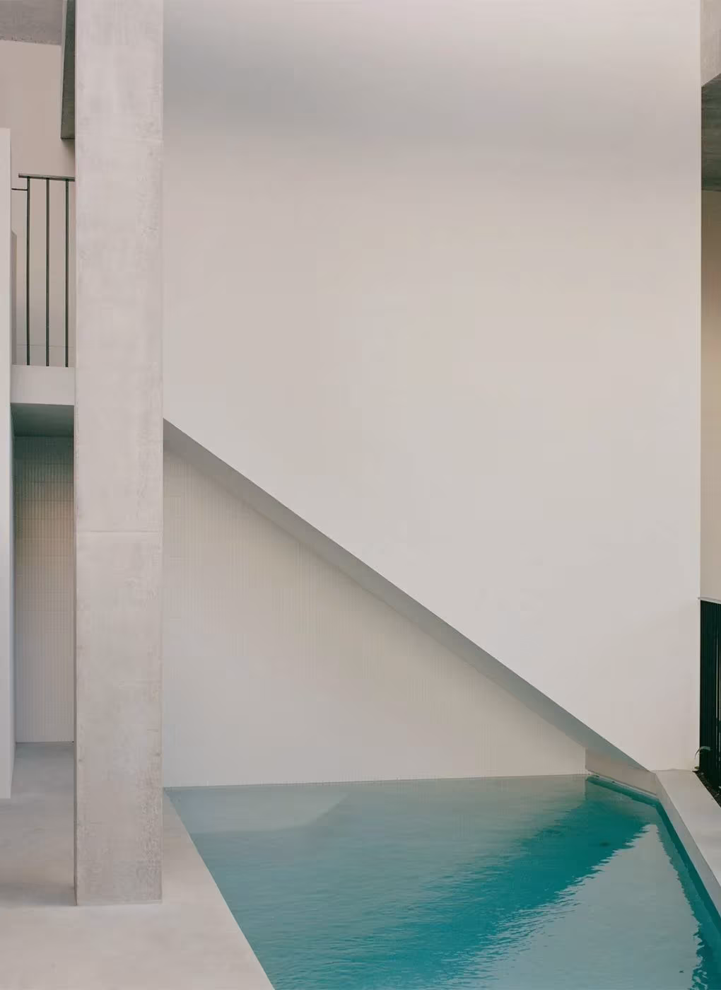 Piscina cubierta de agua turquesa bajo una escalera blanca en la Bronte House de Tribe Studio