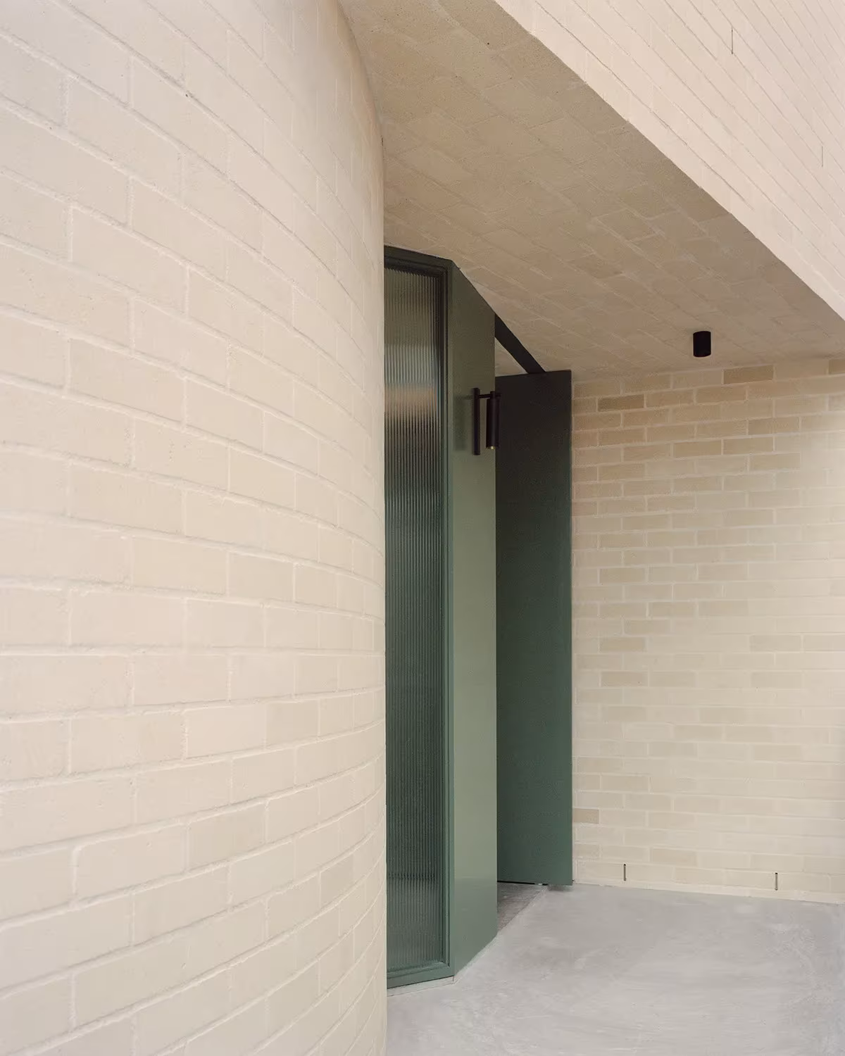Entrada a la Bronte House con muro curvo de ladrillo claro y puerta verde de vidrio