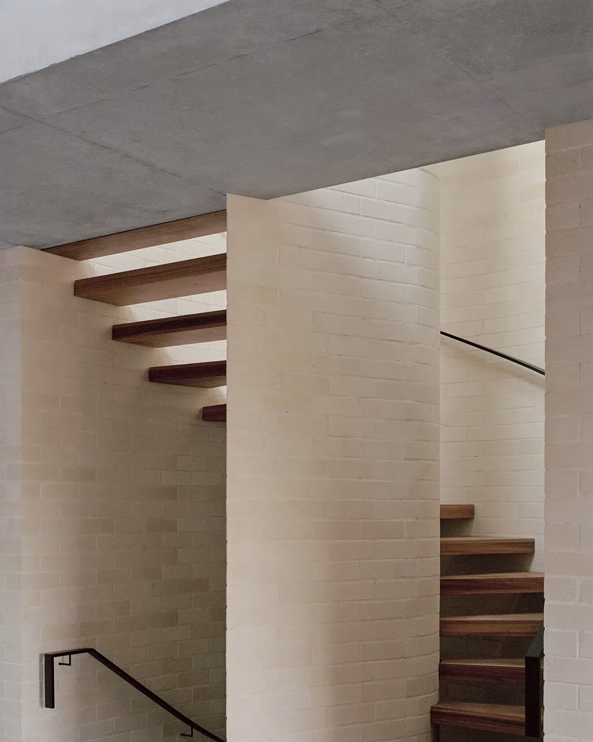 Escalera de peldaños de madera volados entre muros de ladrillo claro en la Bronte House de Tribe Studio