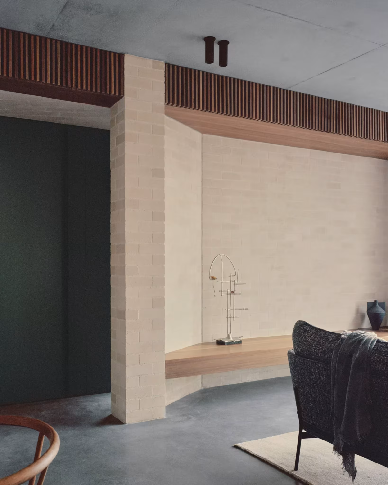 Rincón del salón de la Bronte House con muro curvo de ladrillo, banco de madera y butaca negra