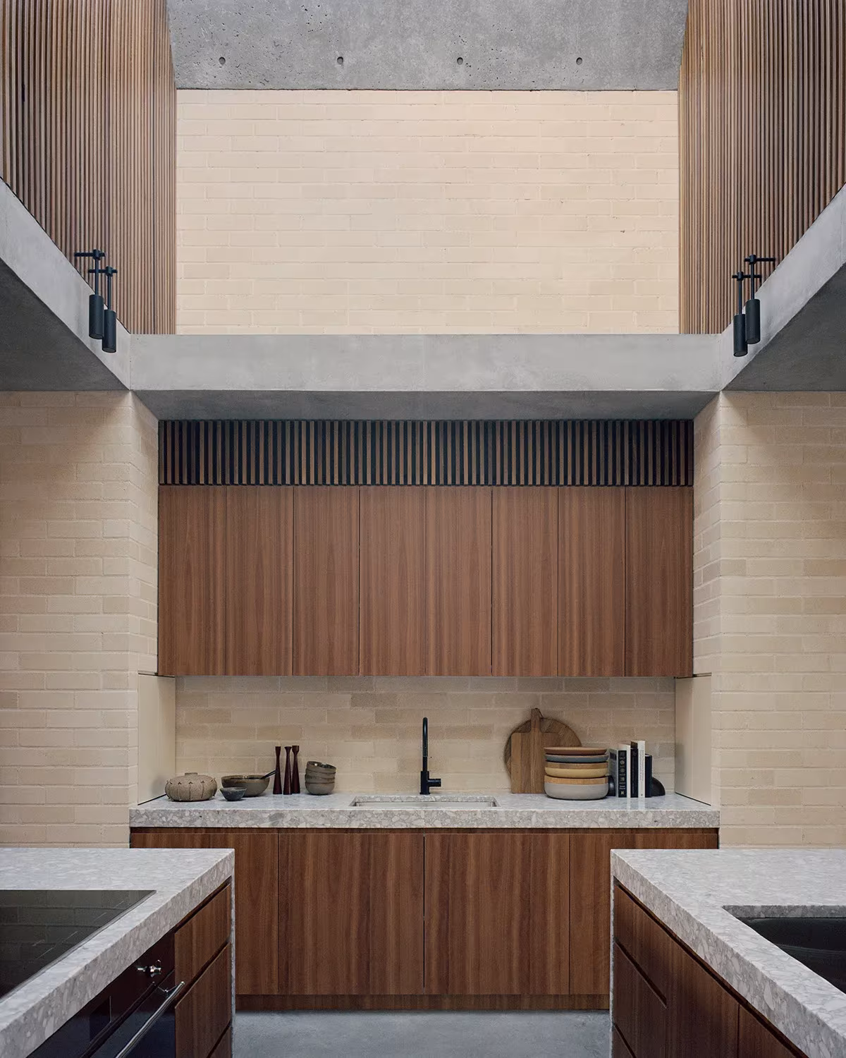 Cocina de doble altura de la Bronte House con frente de madera, ladrillo claro y encimeras de terrazo