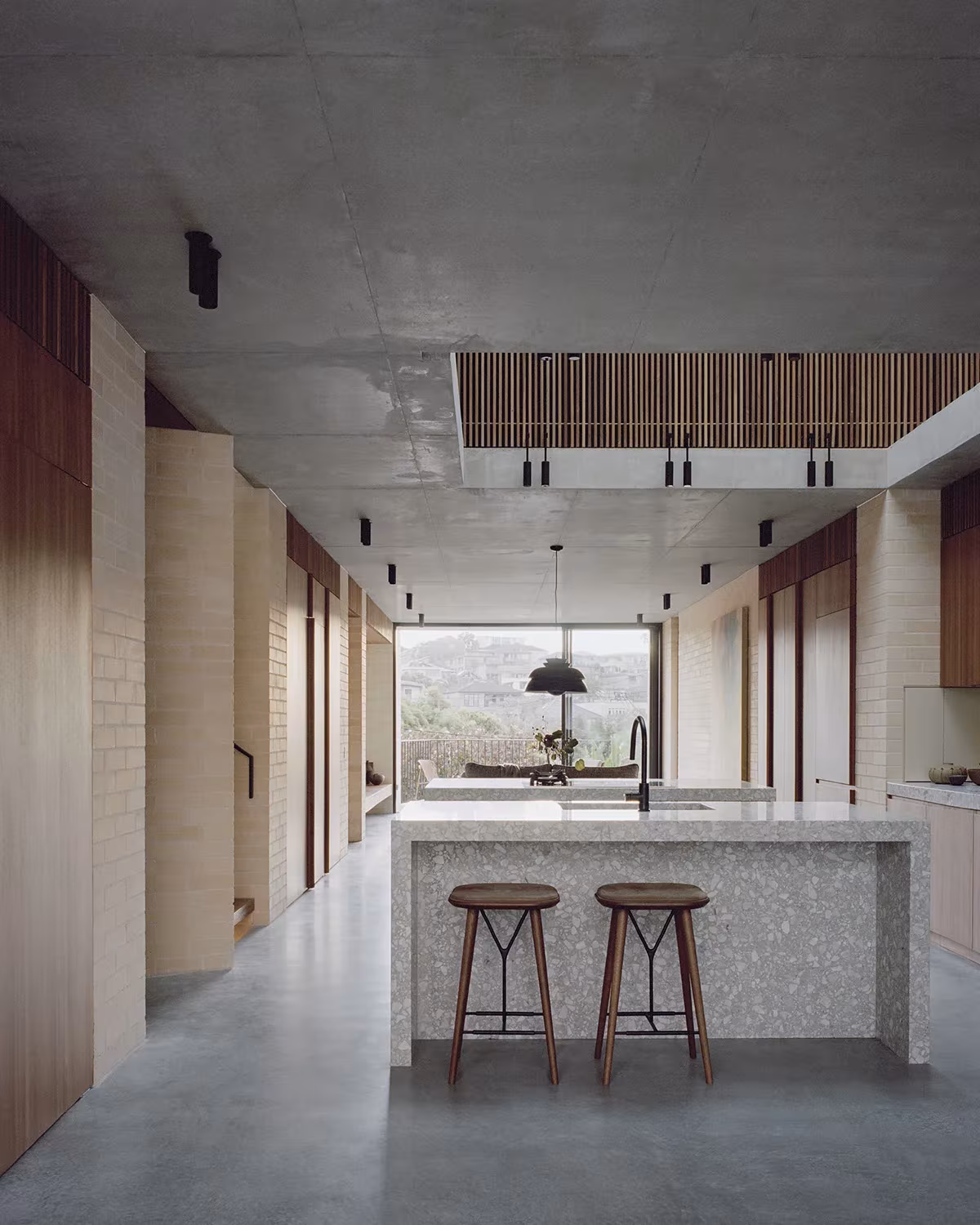 Cocina alargada de la Bronte House con isla de terrazo, taburetes y una gran ventana al fondo