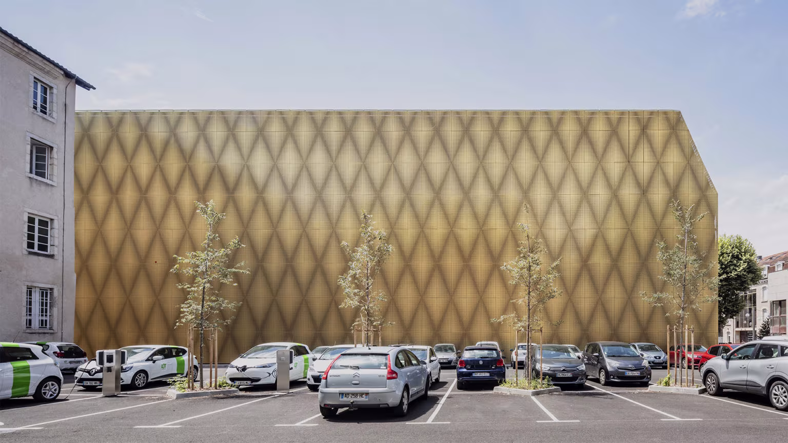 Golden diamond-pattern façade of Le Grand Palais beside a car park and town-centre buildings in Cahors
