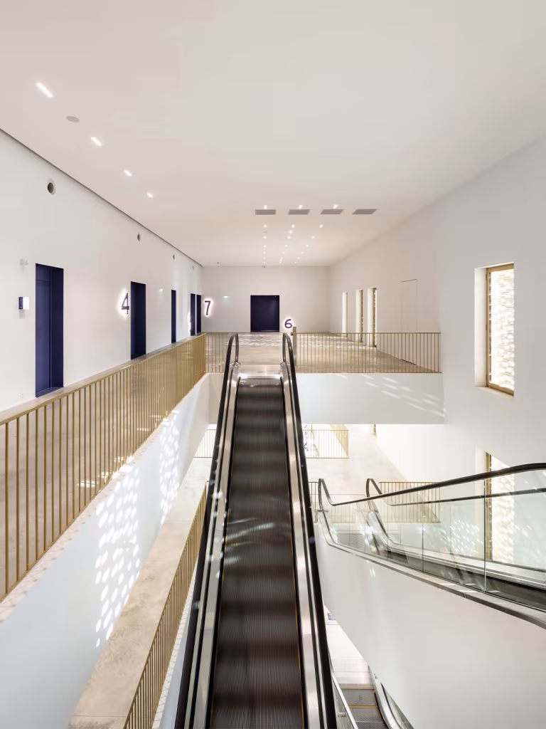White foyer of Le Grand Palais with an escalator, a gold-railed walkway and blue doors